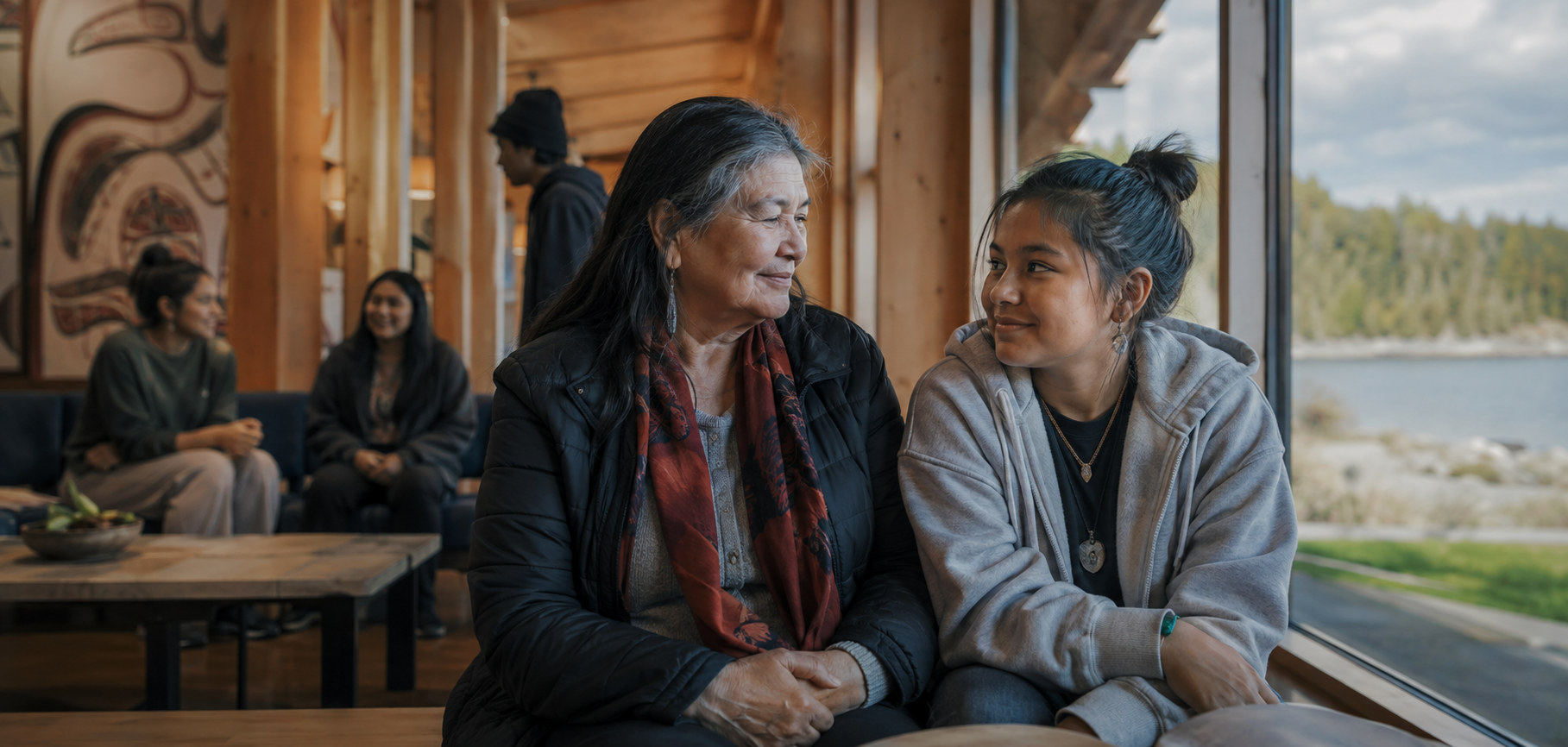 Two women share a conversation in a community building with carved wall panels